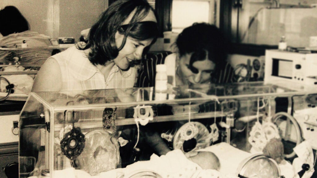 Two women look into a hospital incubator where an infant is lying