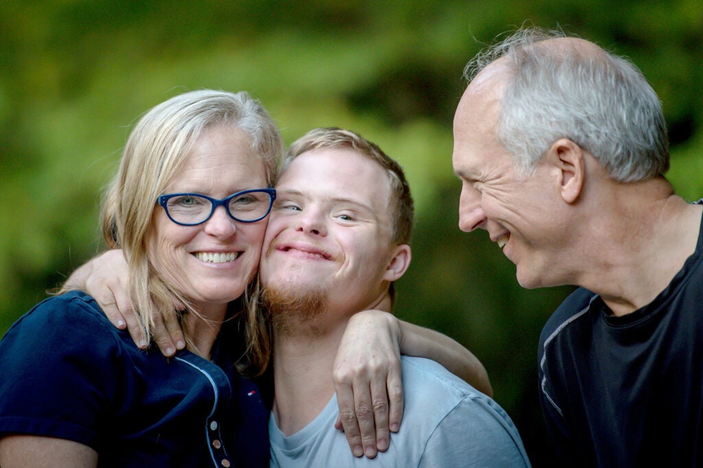 A young man with intellectual disability is hugged by his parents