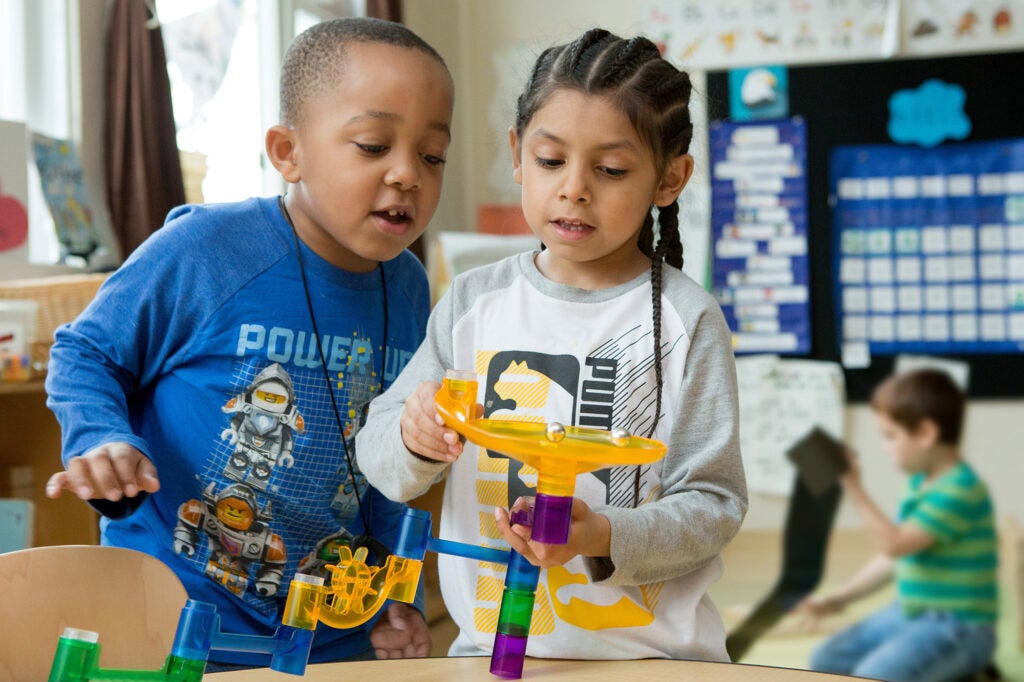 Two young children play with a marble run toy in a classroom