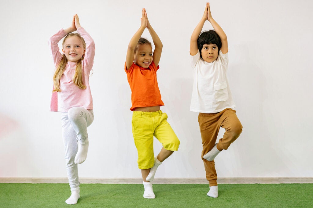 Three young children do tree pose in yoga