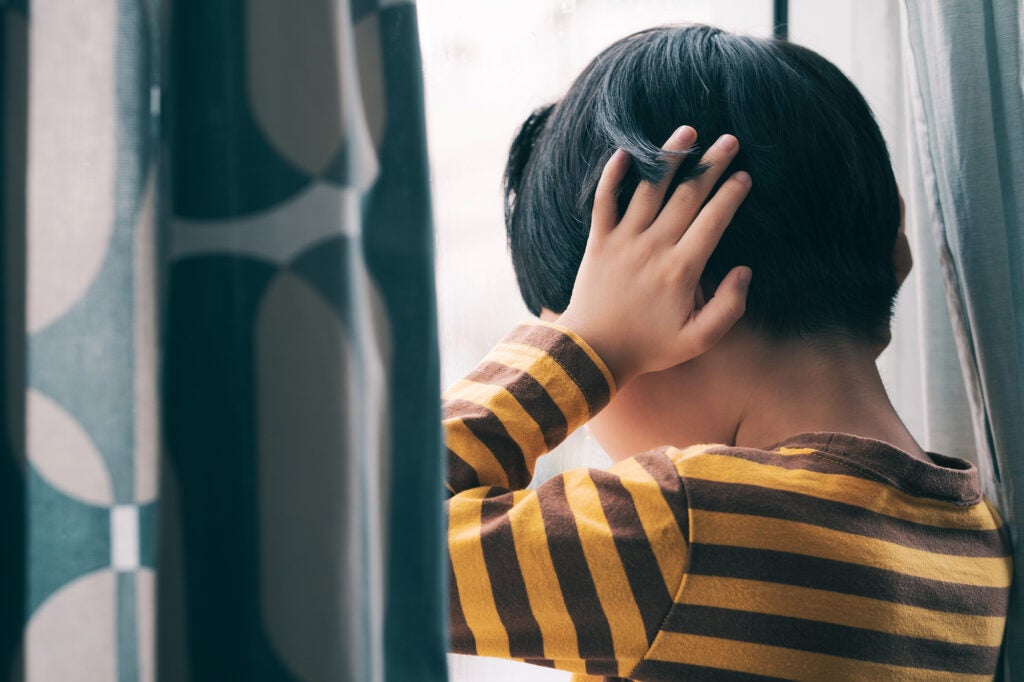 a little boy holds his ears while looking out a window