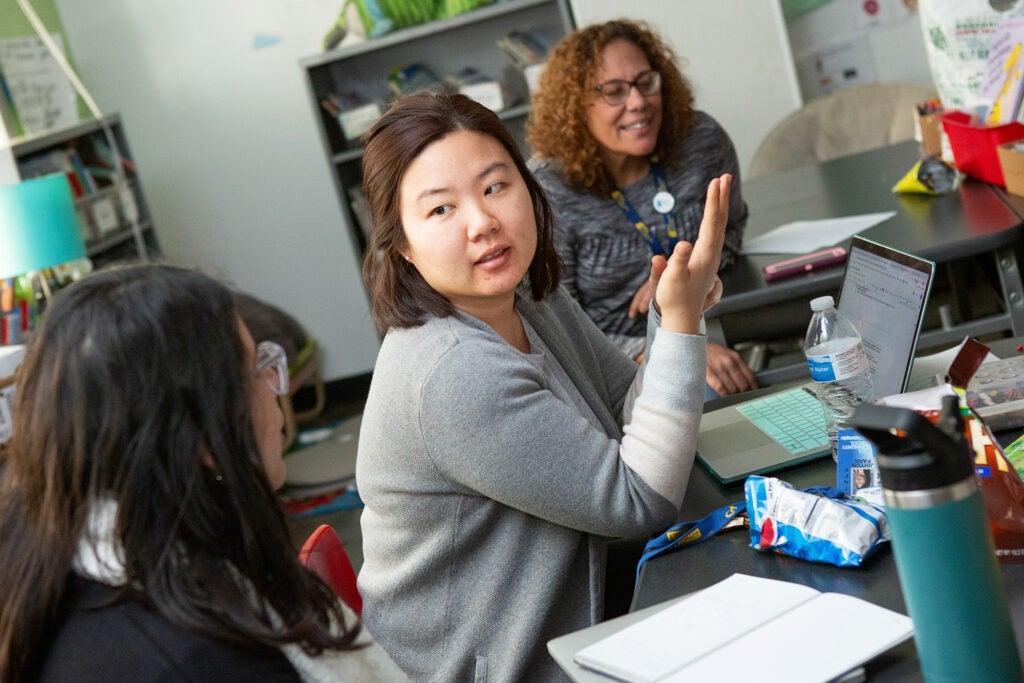 Three teachers talk while creating a lesson plan on a computer