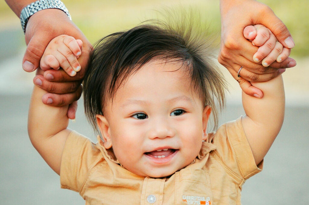 A toddler holds the hands of two adults