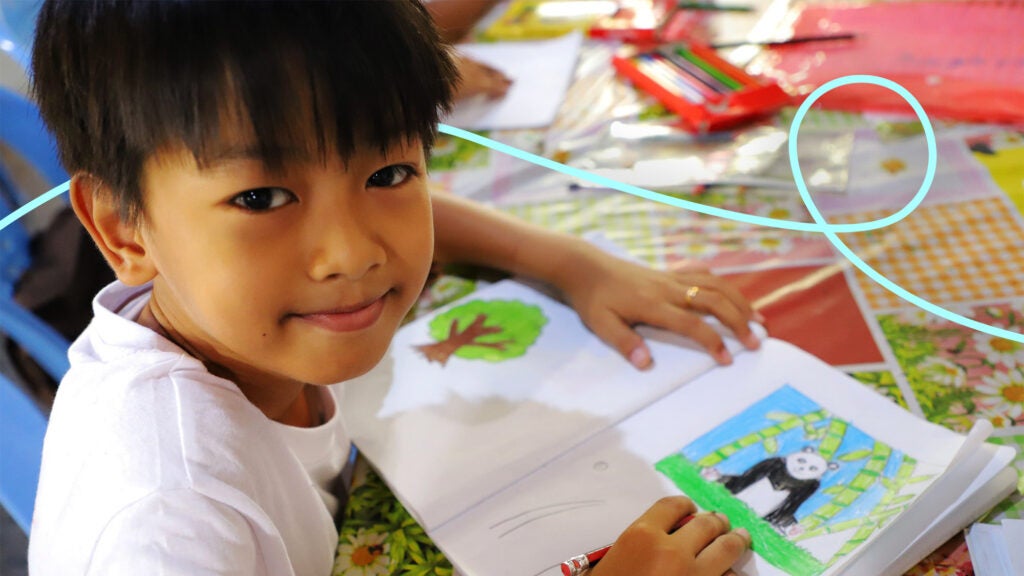 A young Asian boy colors a picture in a book; a line has been added for visual effect