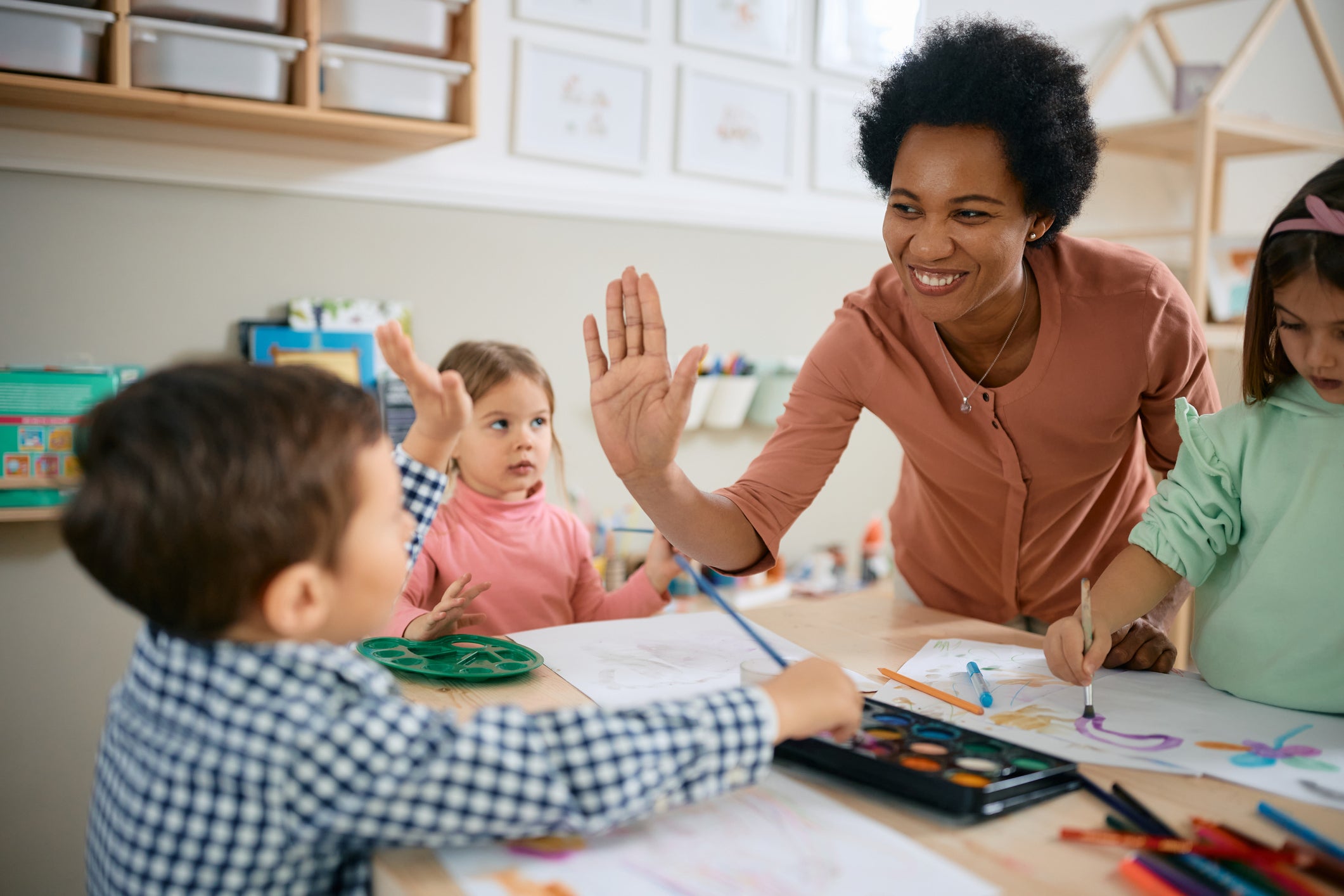 Happy African American teacher and small boy giving high-five during art class at kindergarten